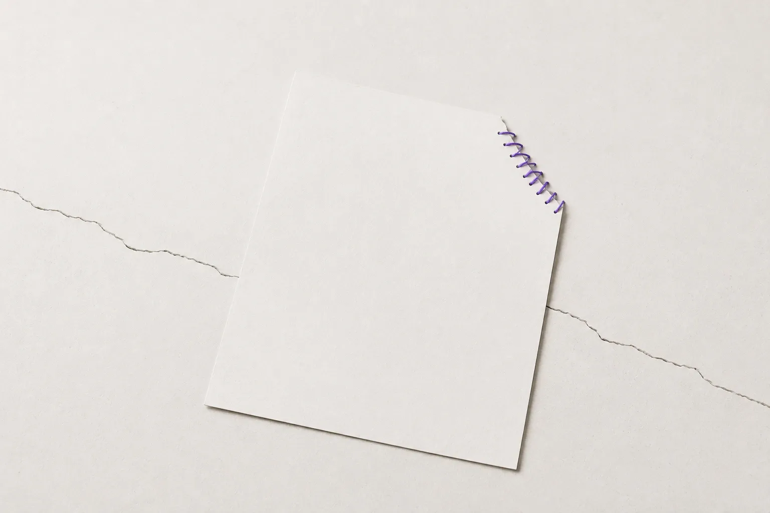 A sheet of paper with one corner mended in violet thread, lying over a crack that runs across the surface beneath it.